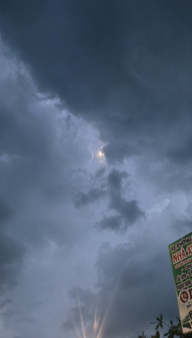 A photograph of a dramatic cloudy sky with lightning and rays of light breaking through, alongside a partial sign with Vietnamese text.