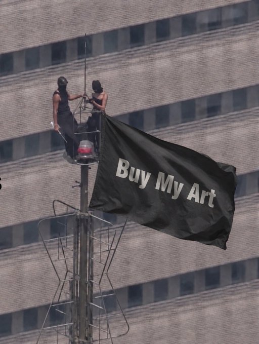 Two people in black clothing stand atop a building or tower attaching a large black flag that reads 'Buy My Art' against a city backdrop.