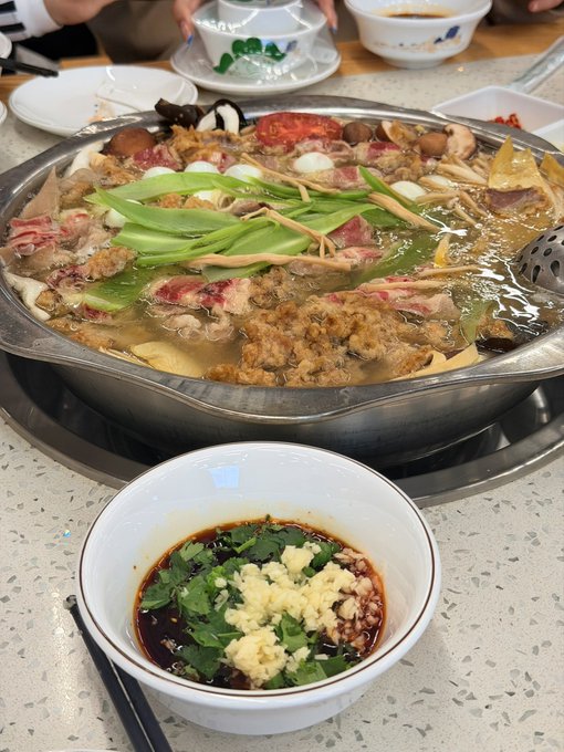 A large steaming pot of boiled vegetables, mushrooms, tomatoes, and meat sits behind a dipping bowl of dark sauce with garlic and cilantro; no readable text or tickers appear in the image. The meal matches the post’s joking “weight-loss meal” theme, though the accompanying text references Lu bro, $AXIS at $0.32, and Evans.