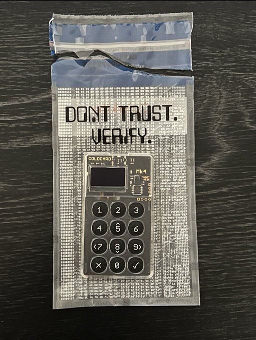 A COLDCARD Mk4 hardware wallet in its sealed anti-tamper packaging with the printed warning "DON'T TRUST. VERIFY." in bold letters.