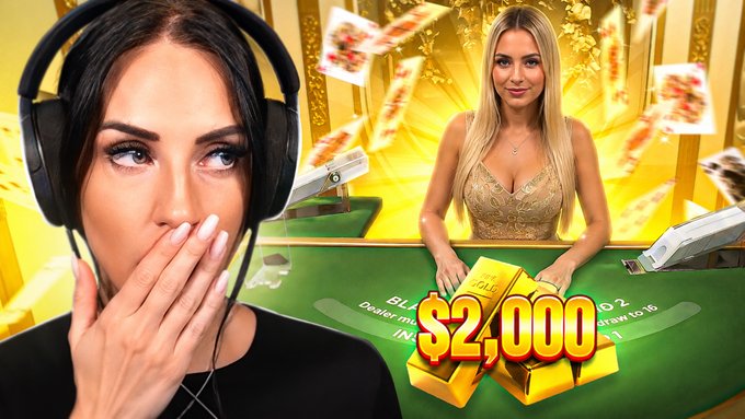 A woman with headphones covers her mouth in shock while watching another woman at a blackjack table, with "$2,000" prominently displayed over gold bars and floating cards. The image promotes a Duelbits blackjack gameplay video, where the viewer reacts to winning $2,000 from a $25 bet.