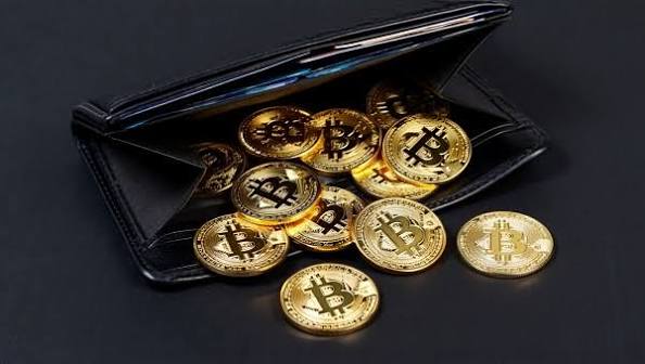 Gold-colored physical Bitcoin tokens spilling out of an open black leather wallet on a dark surface.