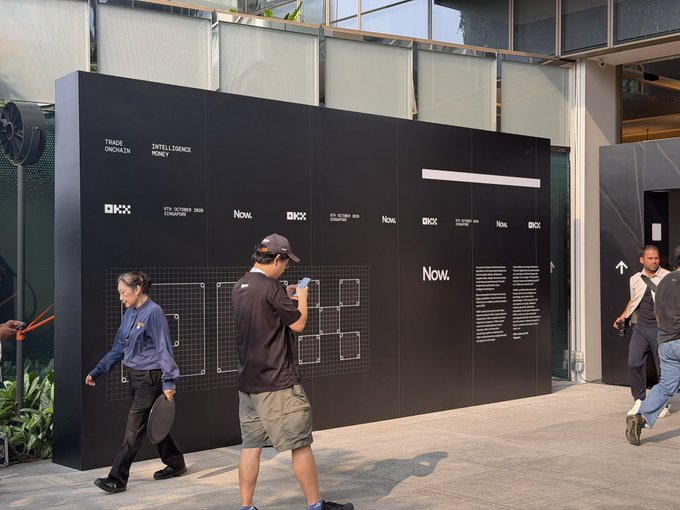 A photograph of an art exhibition entrance shows people walking past a black wall display with 'TRADE ONCHAIN', 'INTELLIGENCE MONEY', 'OKX', and 'Now.' branding, with one person examining a smartphone.