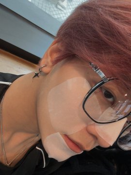 A close-up selfie of a person with pink/red hair wearing black-framed glasses, a star-shaped earring, and clear under-eye patches, looking directly at the camera. The image visually connects to the post's mention of "red hair days," showcasing the person's dyed hair as referenced in their caption asking about showcasing red hair photos.