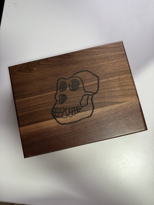 A dark wooden board features a hand-burned etching of a cartoonish monkey skull face.