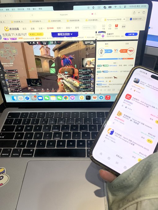 A person holds a smartphone displaying an app interface over an HP laptop keyboard, while the laptop displays a webpage featuring CS gameplay footage and a leaderboard.