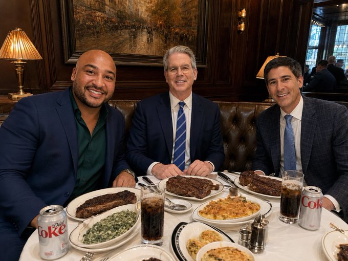 Three well-dressed men smile at the camera while seated around a table at an upscale steakhouse, with plates of steak, spinach, and what appears to be hash browns, along with Diet Coke cans visible in front of them. The setting suggests a casual yet refined business discussion, likely among financial or crypto industry figures discussing Bitcoin's rising value and institutional market dynamics.