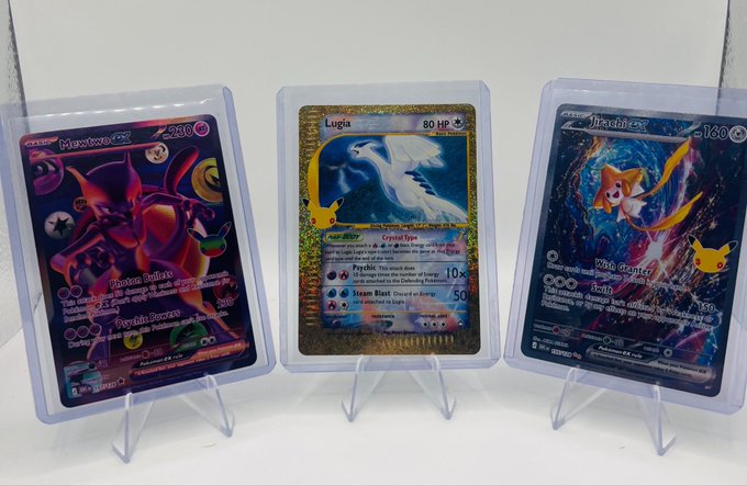 Three Pokémon trading cards displayed on stands: M Mewtwo ex (230 HP), Lugia (80 HP), and M Jirachi ex (130 HP), with the Lugia card featuring a gold holographic background.