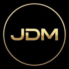 A gold circular logo with the letters 'JDM' on a black background.