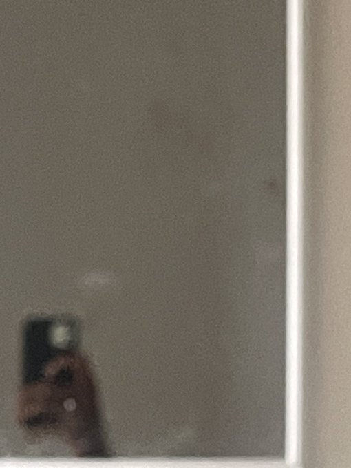 A blurry, dimly lit photo of a person holding up a smartphone, possibly taking a mirror selfie in a low-light environment.