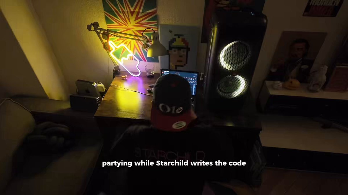 The image shows a person sitting at a desk with a laptop, wearing a red baseball cap and a black shirt. There are two speakers next to them, one of which has neon lights on top that glow green. The room appears to be dimly lit, creating an atmosphere for the party going on in the background. A poster is visible on the wall above the desk, adding to the overall ambiance.