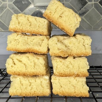 A stack of golden, crumbly shortbread cookies rests on a wire cooling rack, showcasing the homemade treat that the poster learned to bake from @0xSvinci.