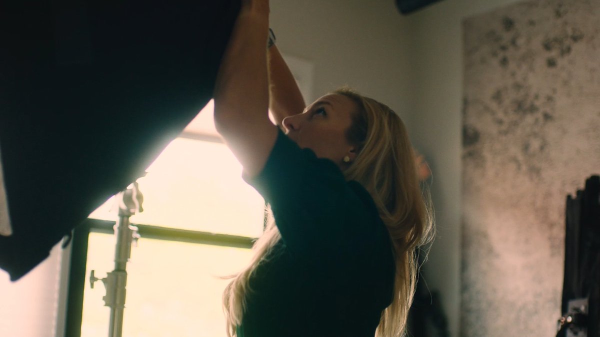 A young woman with long blonde hair reaches upward in a softly lit room, her arms extended as she appears to adjust or hang something out of frame. The image visually represents the "67 million different stories" theme, depicting an individual going about her daily life—the kind of ordinary American moment that the post suggests Congress should keep in mind when considering digital asset regulation.