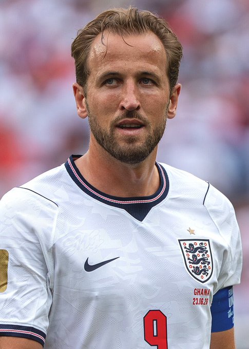 A close-up photo of soccer player Harry Kane wearing the white England national team jersey with a captain's armband and a match tag reading 'GHANA 23.10.22'.