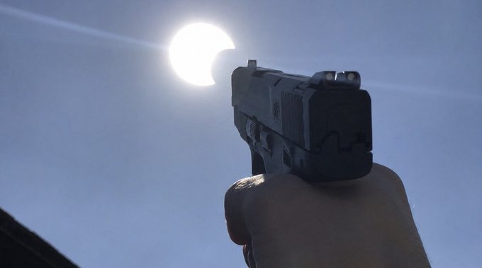 A silhouetted hand aims a handgun toward the bright sun in a clear blue sky, creating a dramatic and cinematic composition. The juxtaposition of the weapon pointed at the sun symbolizes reckless ambition or defiance, fitting the post's tone of unapologetic self-assurance.