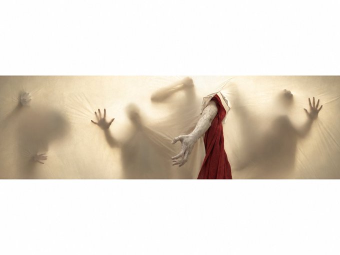 An artistic, surreal illustration showing a figure in a red robe with pale, outstretched hands reaching toward shadowy, faceless figures with their hands pressed against a translucent barrier.