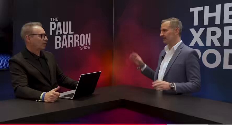 The image shows two men sitting at a table, with one man holding a laptop computer while they are having a conversation about the price of Bitcoin. The other man appears to be discussing the current state of Bitcoin prices or possibly comparing them to a previous time period. There is no visible text in the image that directly relates to the post, but it does provide context for the discussion between the two men.
