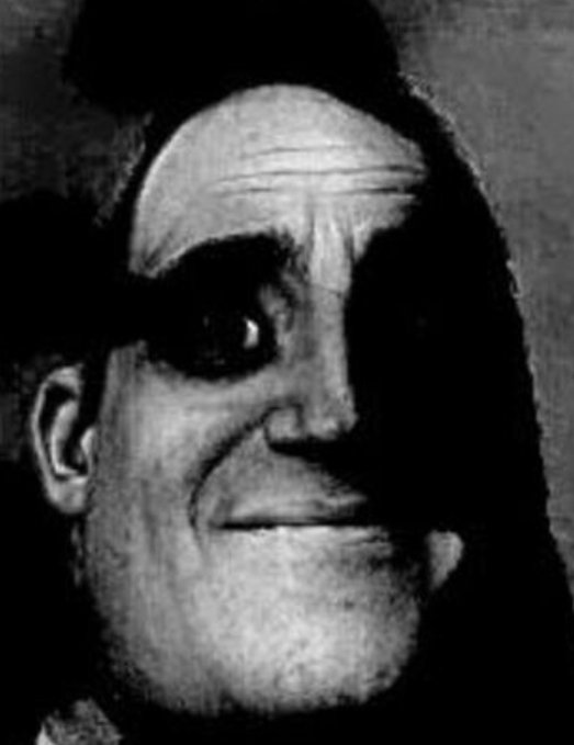 A black and white, eerie image shows a close-up of a man's face with intense eyes and a sinister smile.