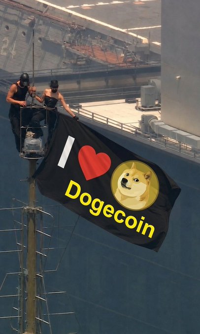 Two people hang a large black "I ❤️ Dogecoin" flag featuring the iconic Shiba Inu Doge meme logo on what appears to be a ship's mast, rallying support for the $DOGE cryptocurrency.
