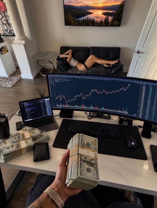 A person holds a thick stack of hundred-dollar bills at a desk with a trading chart on a curved monitor, while stacks of cash sit beside a laptop. In the background, a woman relaxes on a couch, reinforcing the post's message of how quickly life can transform from nothing to success.