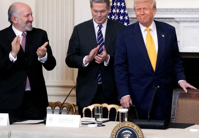 Three men in business suits stand together at an event, with two of them applauding; a nameplate partially reads 'Scott Bessent' near a Vice Presidential seal.