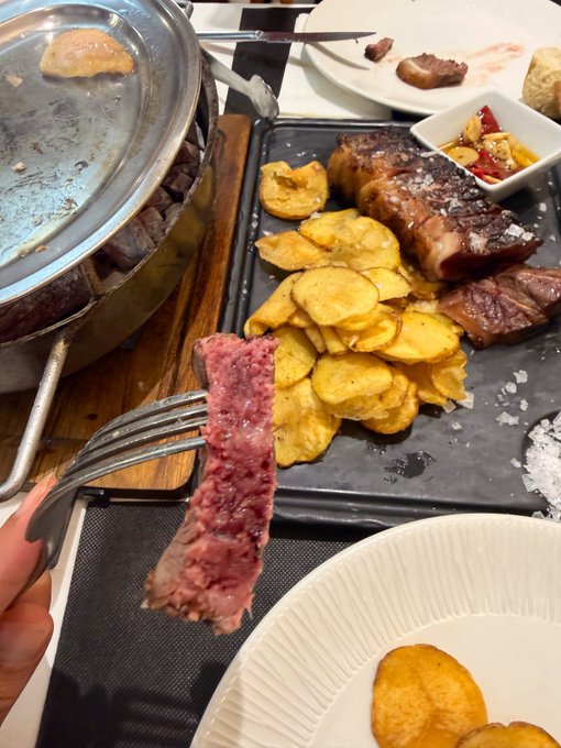 A juicy, perfectly pink slice of steak is held up on a fork, fresh from the sizzling grill pan, ready to be paired with crispy golden potato slices. The image embodies the caption's emphasis on steak done exactly right—medium-rare, tender, and cooked to perfection without compromise.