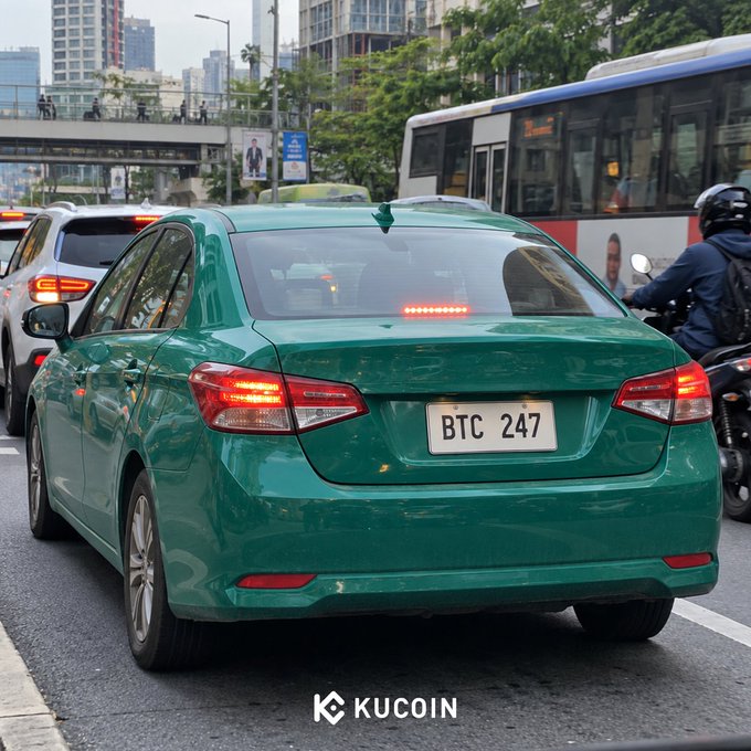 A green sedan with license plate “BTC 247” drives through city traffic beside a bus and motorcyclist. The “KUCOIN” logo appears at the bottom, matching the post’s reference to BTC, ETH, and other cryptocurrencies available on KuCoin Spot.