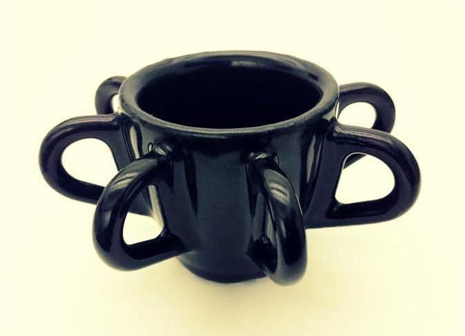 A black ceramic cup or vessel with multiple curved handles extending outward from its sides, photographed against a light background.