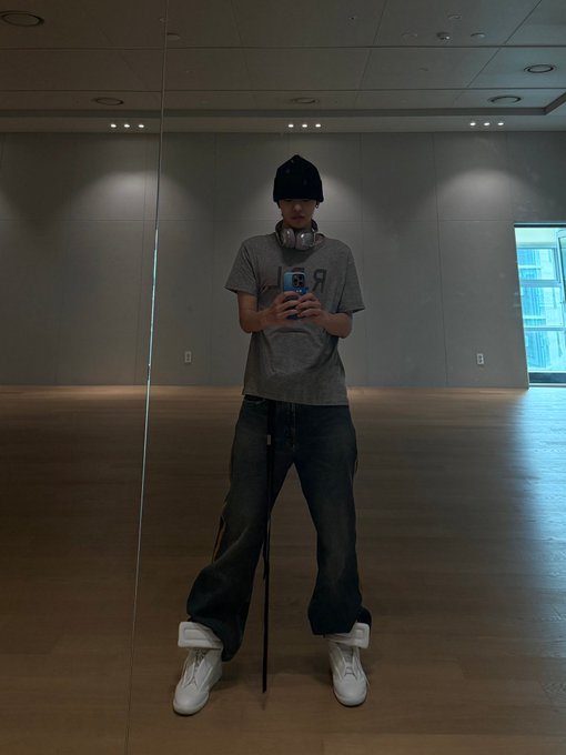 A person wearing a black beanie, gray t-shirt, baggy dark jeans, and white sneakers takes a mirror selfie with a phone while holding a long object, standing in a minimalist room with recessed ceiling lights.

The image accompanies the post "260714 plus chat update let's keep going today too #LEO #리오," suggesting it documents a casual daily update or lifestyle moment shared by someone identified with the handle "LEO" or "리오."