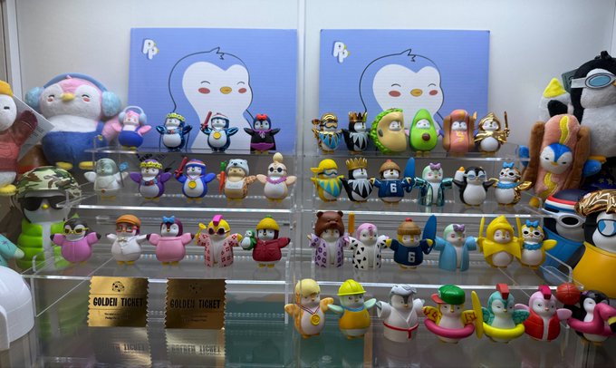 A display case shows a collection of various penguin figurines in different costumes and outfits, arranged on tiered shelves with "GOLDEN TICKET" cards visible.