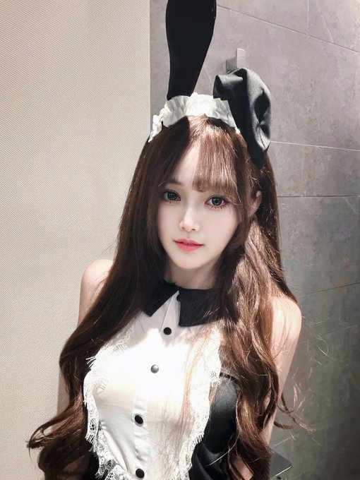 A young woman with long brown hair poses in a black and white maid-style outfit, complete with bunny ears headband, against a tiled wall in softly lit indoor lighting that captures the quiet mood of "Night."