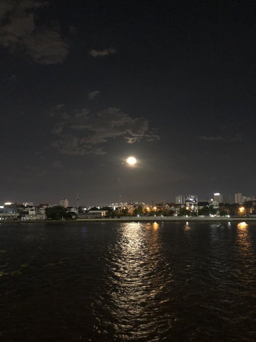 A nighttime view of the moon reflecting on water with a city skyline in the distance.