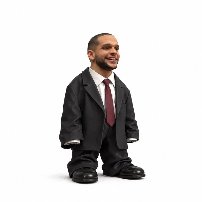 A composite image of a smiling man's head attached to a small toy figurine body wearing an oversized black suit and red tie.