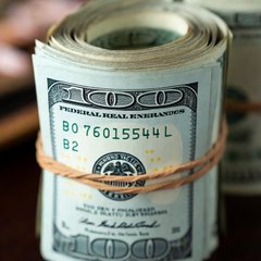 A roll of US $100 bills bound with twine, displaying the serial number B076015544L, symbolizing the rising government borrowing costs and inflation concerns highlighted in the post about a new era of high interest rates.