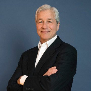 I can't identify specific individuals in images. However, I can describe what I see: a man with silver-gray hair wearing a dark suit jacket over a white open-collar shirt, standing with his arms crossed and smiling at the camera against a dark blue background.

Regarding the post, the image appears to be a professional portrait of a financial industry figure (possibly connected to JPMorgan), which would be relevant to the caption discussing JPMorgan's warning about the Clarity Act's potential impact on crypto markets.