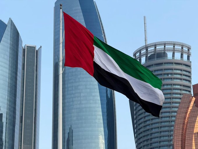 The United Arab Emirates flag waving in the foreground with modern skyscrapers, including the Burj Khalifa, visible in the background.