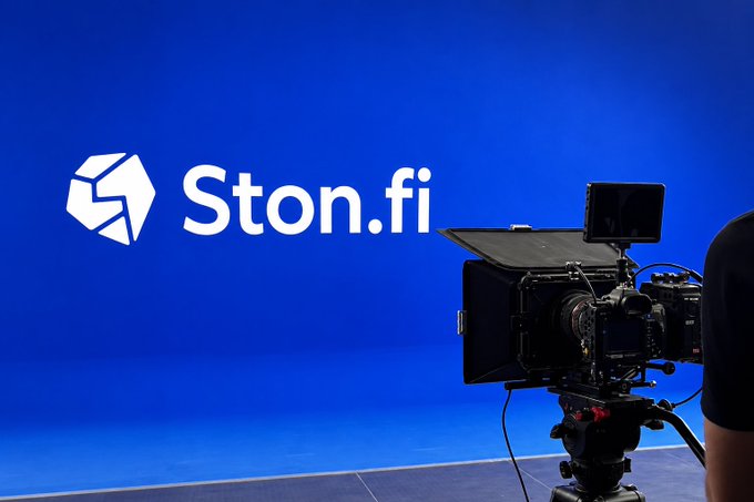 A professional video camera positioned in front of a blue screen displaying the white 'Ston.fi' logo and branding.