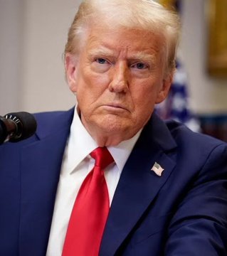 A portrait of Donald Trump in a blue suit with a red tie, sitting in front of a microphone.