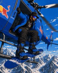 Person dressed in black gear and a cowboy hat standing on the skid of a Red Bull helicopter above snowy mountains.