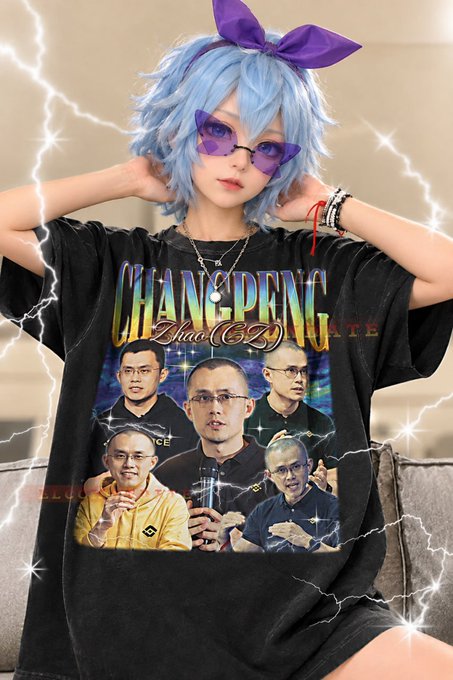 A person with light blue hair and a purple bow wears a black t-shirt featuring a 'CHANGPENG ZHAO (CZ)' graphic with multiple images of the Binance founder, edited with anime-style filter effects.