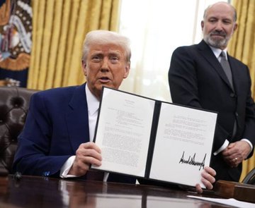 In the image, Donald Trump holds up a document in the Oval Office, an apparent signing ceremony that relates to the accompanying post's claim of a US CBDC ban bill becoming law.