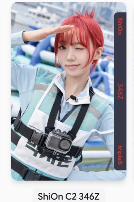 A photo card featuring ShiOn from tripleS, with red hair and a teal and white outfit, saluting while wearing a chest-mounted camera. The card is labeled 'ShiOn C2 346Z'.