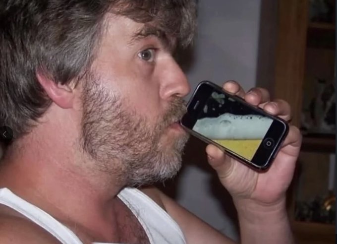 A close-up of a man holding a smartphone showing an image up to his mouth, appearing to lick or kiss the screen.