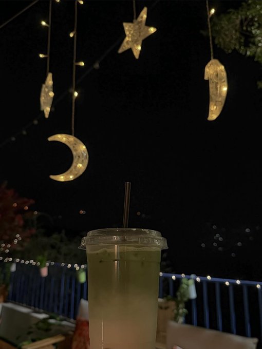 The image features a cup of tea with a straw, placed on a table outside at night. The scene includes lights hanging from strings above the table, creating an enchanting atmosphere. There are also stars visible in the background, adding to the overall ambiance. The caption for the image reads "Good night Frens See y'll tomorrow Can I get GN back?" and "@quipnetwork @CNPYNetwork @useTria".
