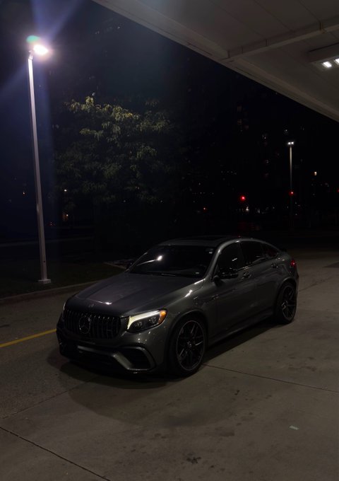 A dark gray Mercedes-Benz coupe parked at night under a streetlight beneath an overpass or building overhang.