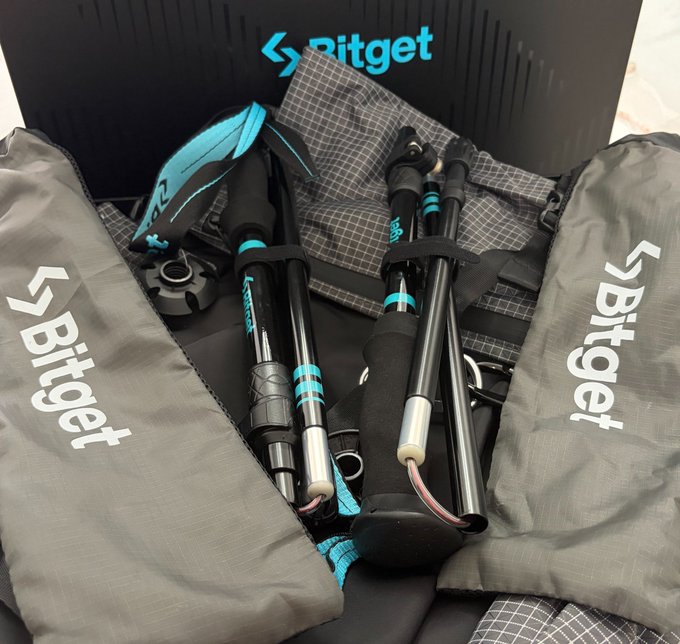 A user unboxes the Bitget 8th Anniversary gift box, revealing a stylish gray backpack and a pair of teal-accented hiking poles branded with the "Bitget" logo, perfect for their upcoming weekend hiking trip.