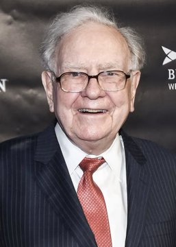 Photograph of an elderly smiling man in a dark pinstripe suit, white shirt, and red tie, wearing glasses, appearing at a formal event.