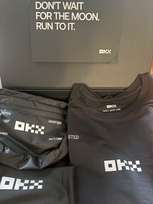 Black athletic apparel and accessories from the brand OKX, including a shirt with 'BUILT WITH LOVE' tag, displayed with a motivational card reading 'DON'T WAIT FOR THE MOON. RUN TO IT.'