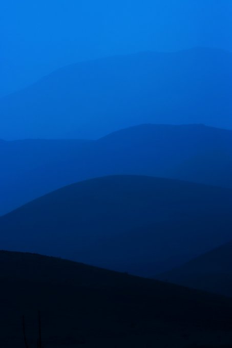 A layered minimalist illustration of rolling hills rendered in gradient shades of deep blue, with progressively darker silhouettes fading into the distance.