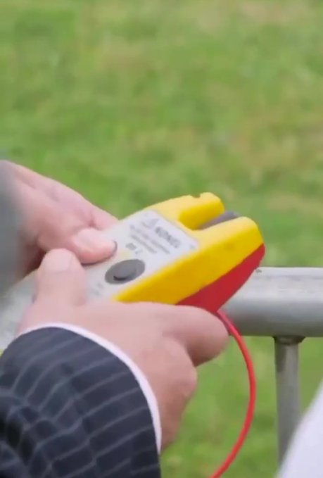 A person holds a yellow device with a red cord against a metal railing on grass, appearing to be in the act of pressing or resetting the device. The image symbolically aligns with the post's message of "resetting the outdated financial system," visually representing the act of initiating a reset.